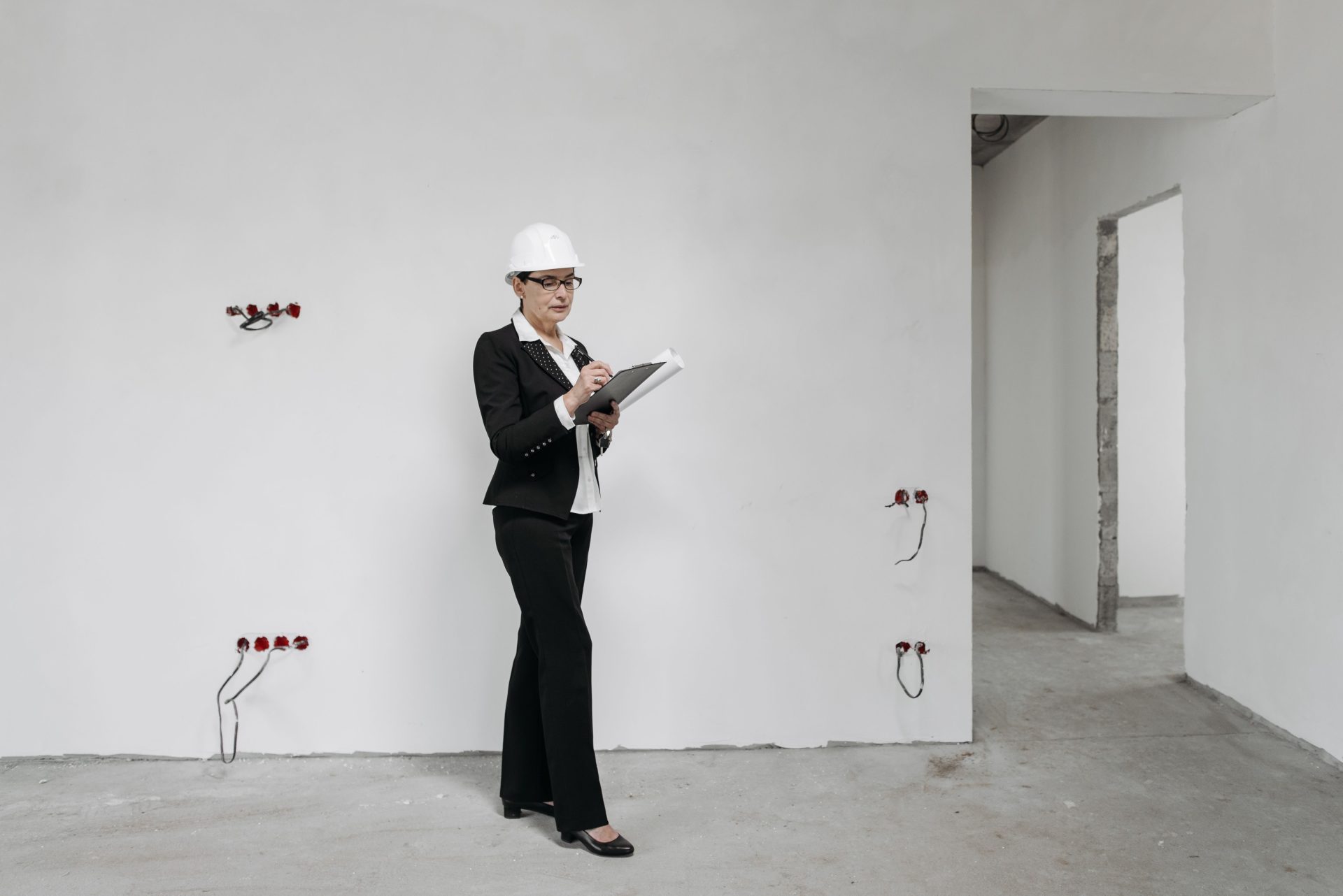 Eine Frau mit Schutzhelm prüft auf einer Baustelle ihre Notizen und begutachtet den Baufortschritt.